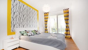 A modern bedroom with a large bed, a nightstand, a wall art piece, and a window with curtains. - Golden Sun Apartments- Polanki (Kolobrzeg)