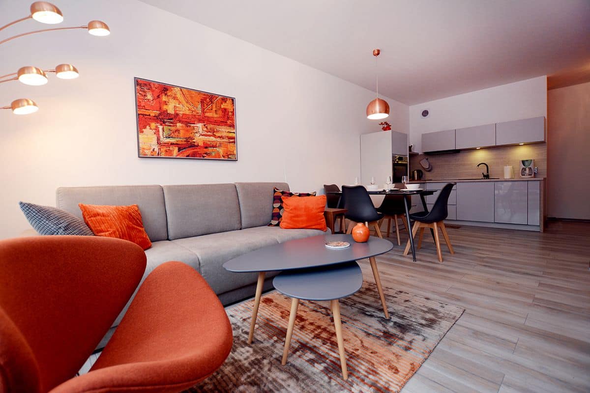 A modern living room with a grey sofa, orange and blue cushions, a round coffee table, and a patterned rug.