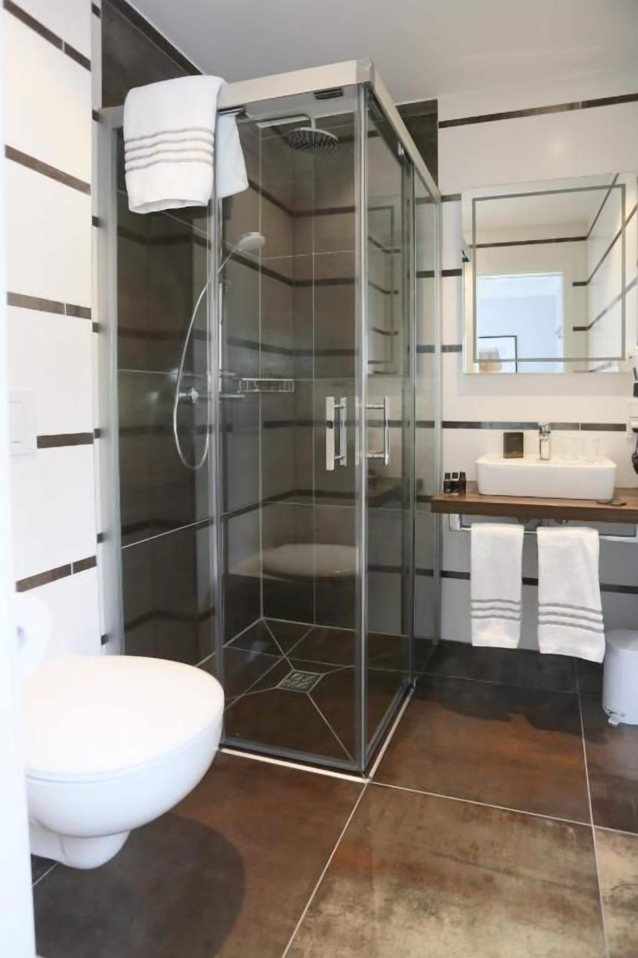 Un baño moderno con ducha envuelta en vidrio, inodoro blanco y lavamanos con espejo.
