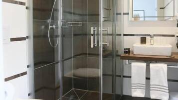 Un baño moderno con ducha envuelta en vidrio, inodoro blanco y lavamanos con espejo.