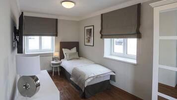 Quarto com cama, mesa de cabeceira, abajur e janela com cortinas.