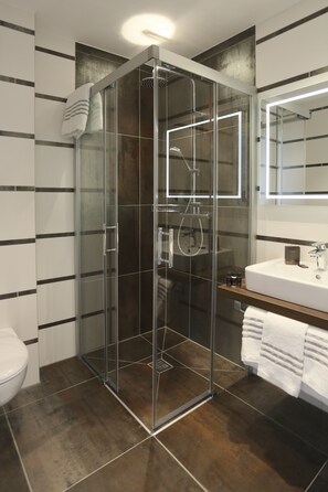 Un baño moderno con ducha envuelta en cristal, lavamanos blanco y espejo grande.