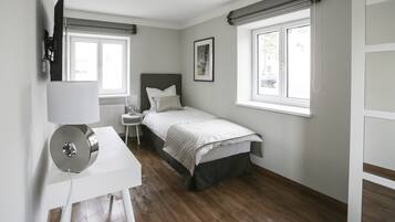 A bedroom with a bed, a desk, a lamp, and a window.