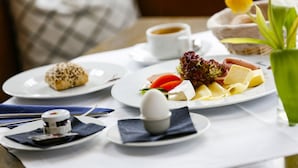 A breakfast setting with plates of food, a cup of coffee, and a vase with tulips. - Hotel zur Schloss-Schmiede (Kühbach)