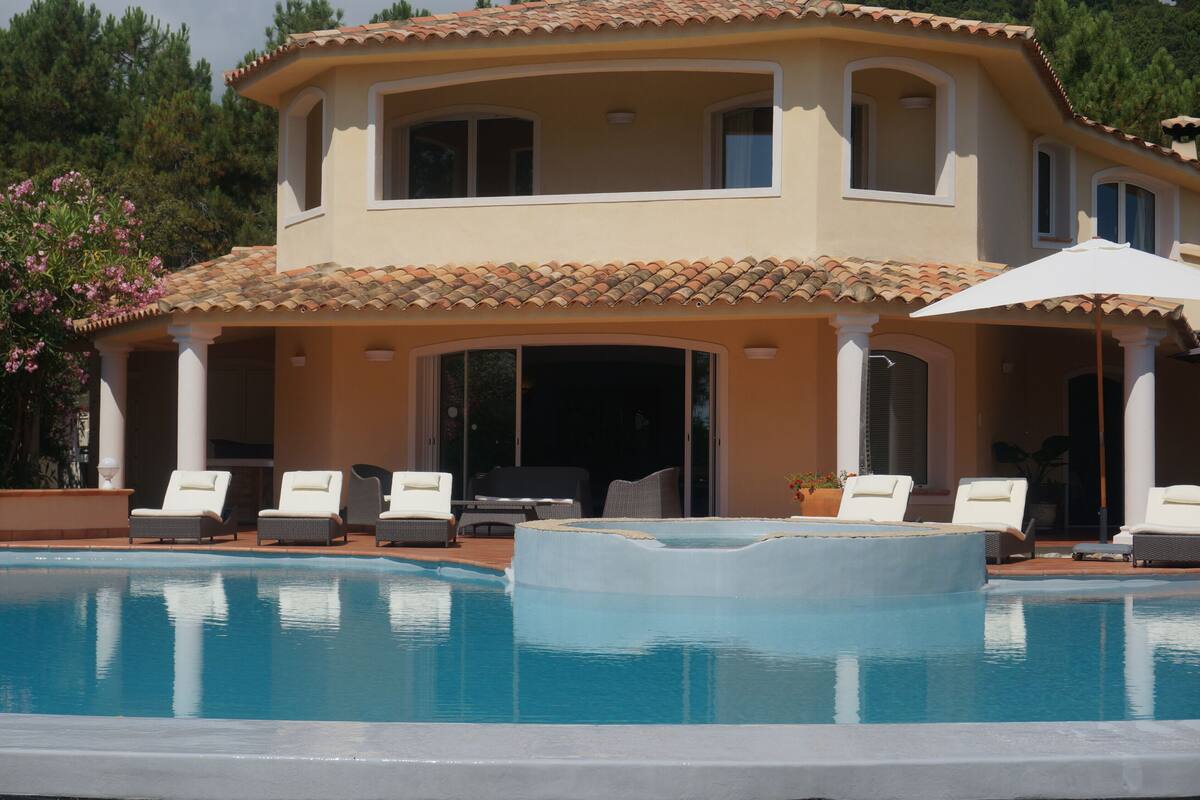 Ein zweistöckiges Haus mit Pool, Sitzgelegenheiten im Freien und einer überdachten Terrasse.
