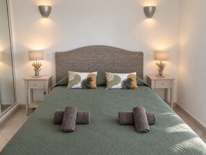 A neatly made bed with a green bedspread, two pillows with leaf patterns, and two rolled towels.