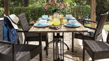 Un espace de restauration en plein air, avec des chaises en osier et une table dressée avec des assiettes, des bols et une carafe de limonade.