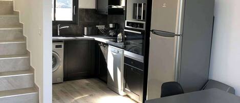 A modern kitchen with a built-in oven, a refrigerator, and a dining area with a table and chairs.