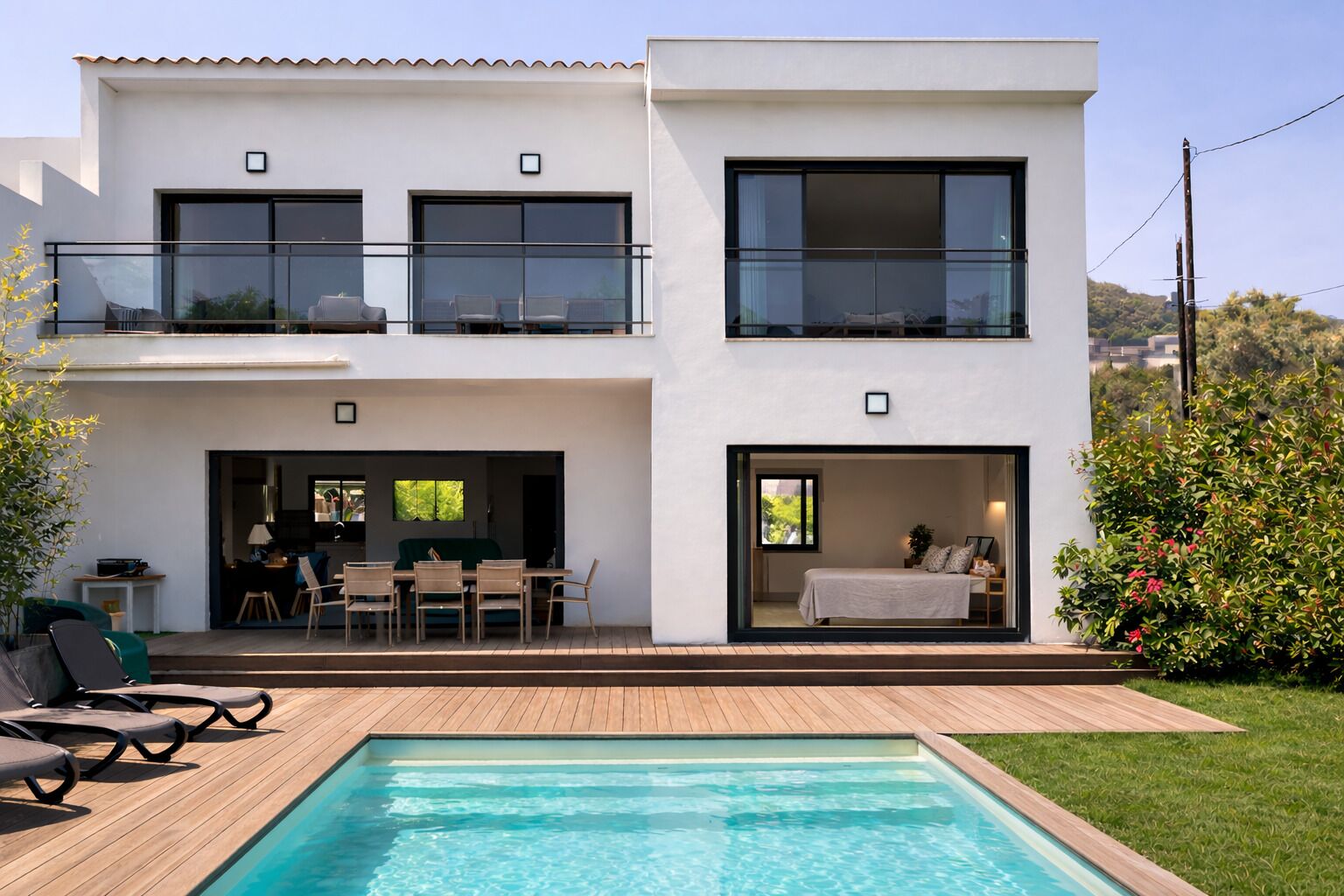 Ein modernes, zweistöckiges Haus mit Schwimmbad, Sitzgelegenheiten im Freien und einem Balkon.