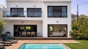 A modern two-story house with a swimming pool, outdoor seating, and a balcony.