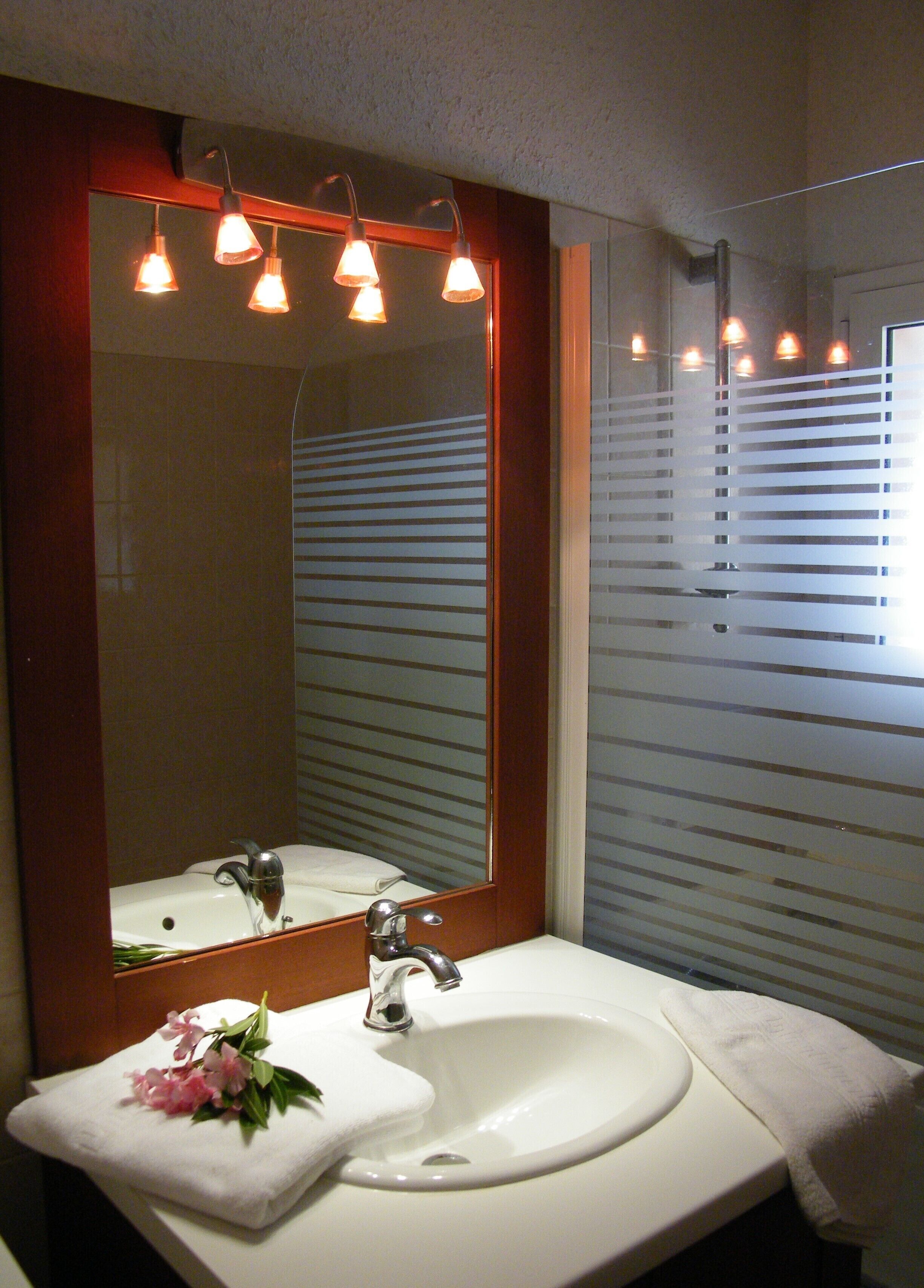 Un baño con un lavabo blanco, un espejo con marco de madera y una ventana con persianas horizontales.