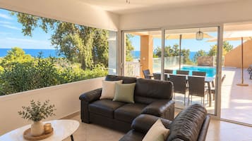 Een moderne woonkamer met een leren bank, een bijzettafeltje en uitzicht op zee door grote ramen.