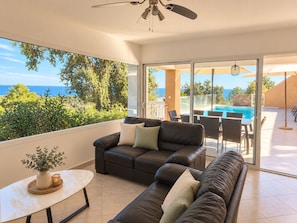 A modern living room with a leather sofa, a small table, and a view of the sea through large windows. - Mare e Monte (Sari-Solenzara)