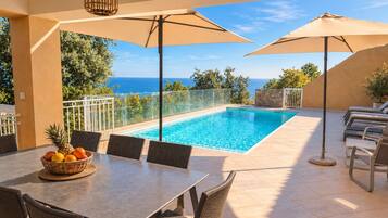 A poolside area with a table, chairs, and umbrellas.