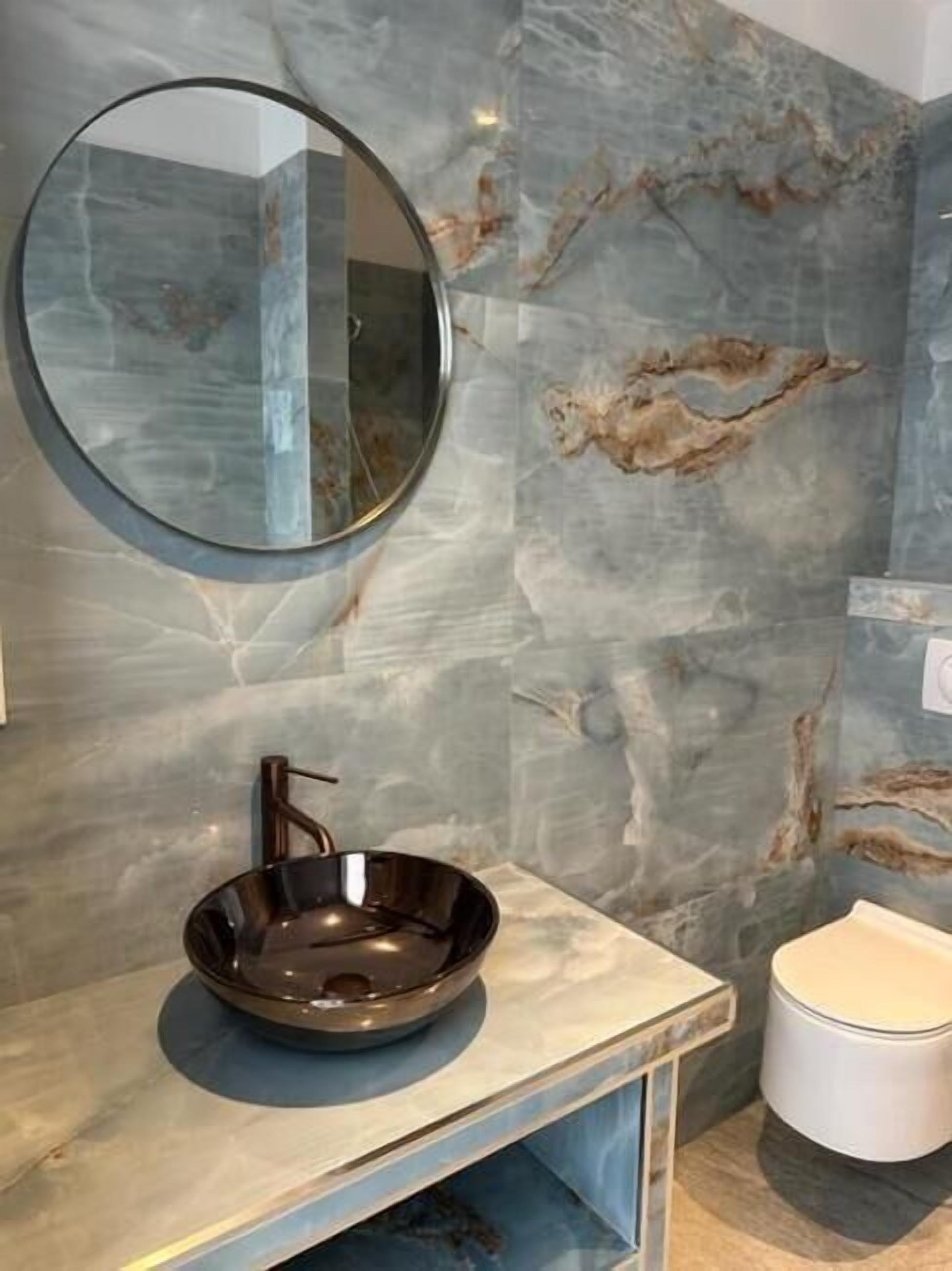 Ein Badezimmer mit rundem Spiegel, einem Waschbecken und einer Toilette.