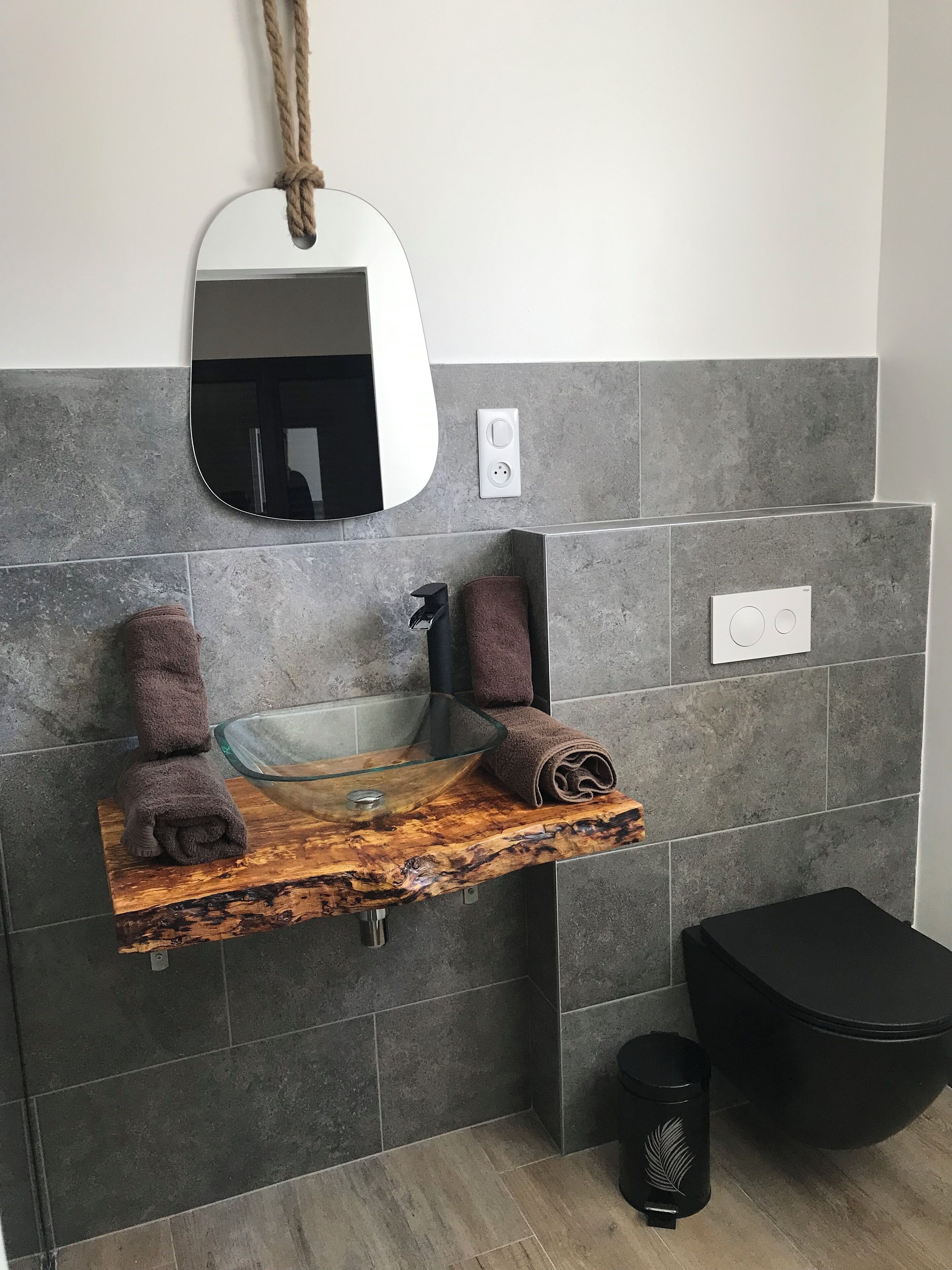 Une salle de bain avec un lavabo en verre, deux serviettes, un miroir et une poubelle noire.