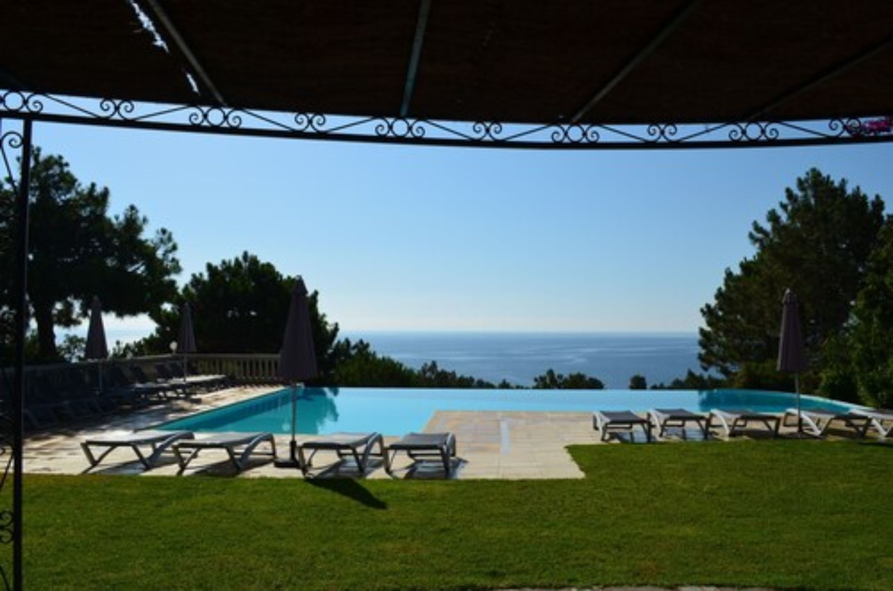 A pool area with a view of the ocean, surrounded by lounge chairs and umbrellas.