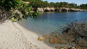 A beach with clear shallow water, sandy shore, and rocky outcrops. - Mare e Monte (Sari-Solenzara)
