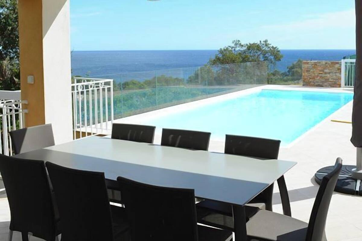 Ein moderner Essbereich im Freien mit Pool und Meerblick.