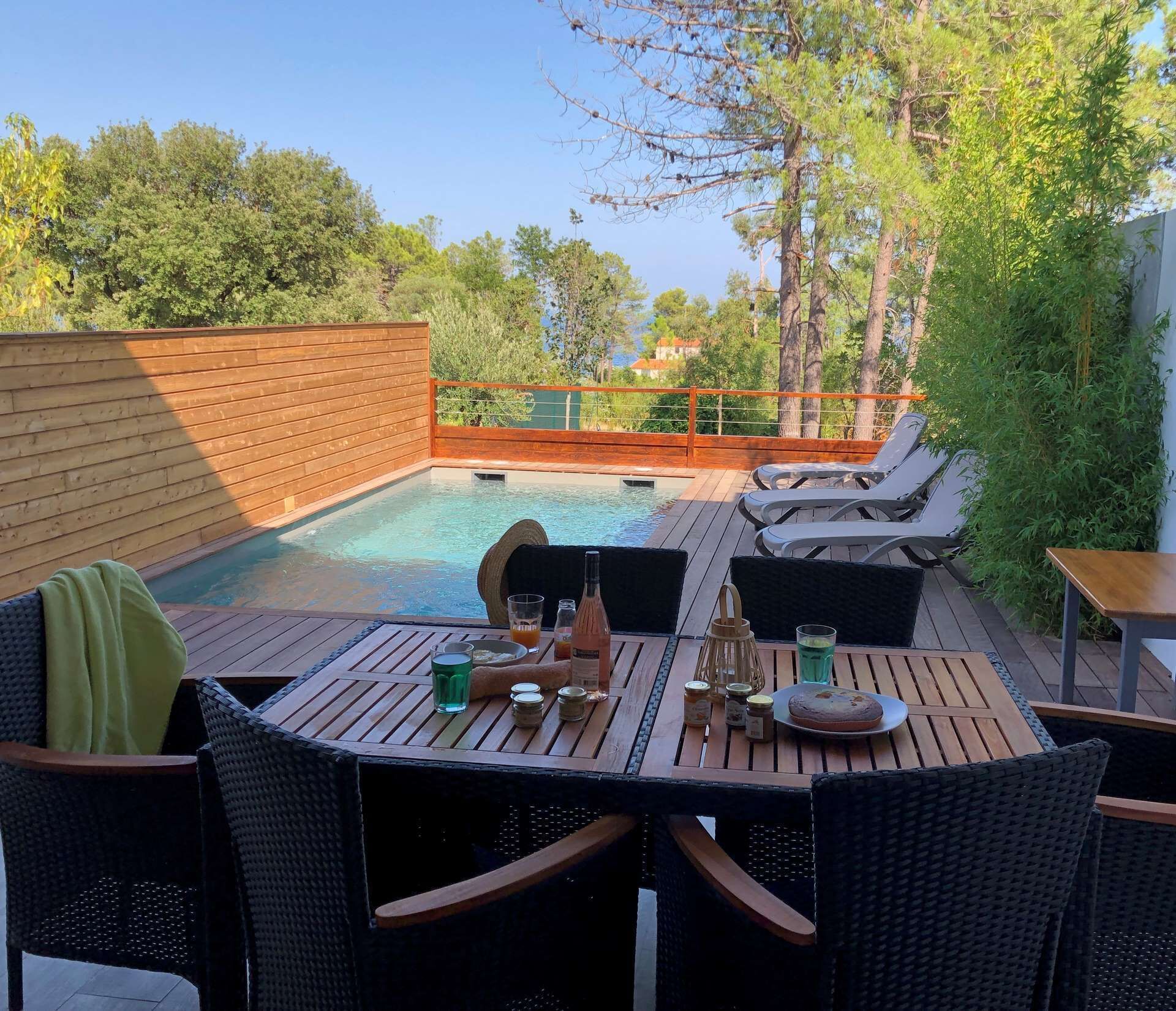 A wooden deck with a pool, lounge chairs, and a table set with drinks and condiments.