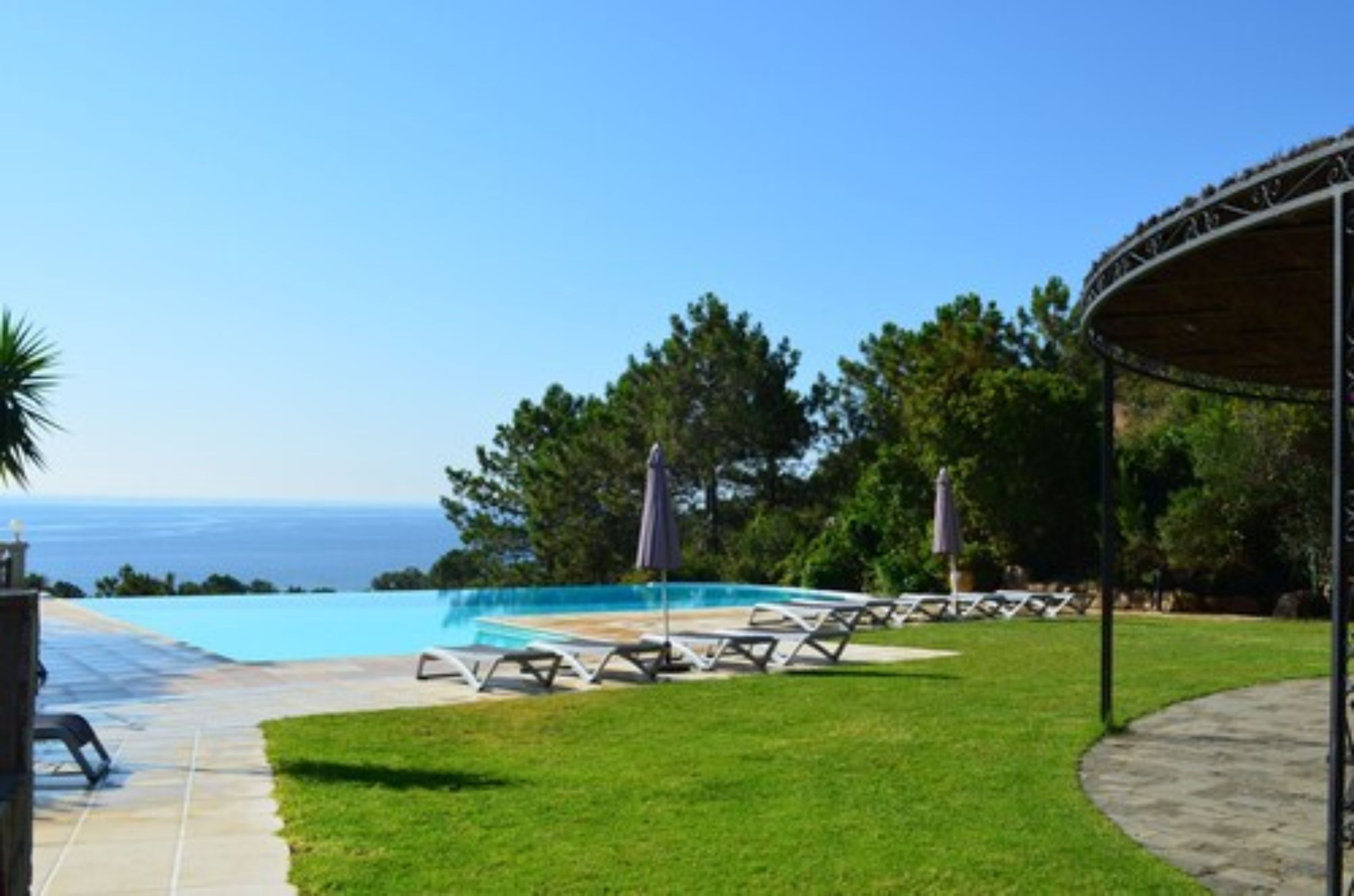 A pool area with lounge chairs and umbrellas, a covered seating area, and a view of the ocean.