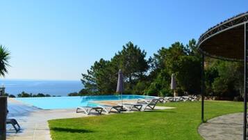 A pool area with lounge chairs and umbrellas, a covered seating area, and a view of the ocean.