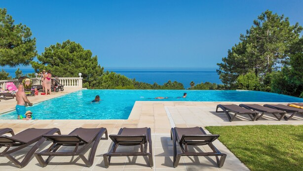 A swimming pool with a view of the sea, surrounded by lounge chairs and a deck area. - Mare e Monte (Sari-Solenzara)