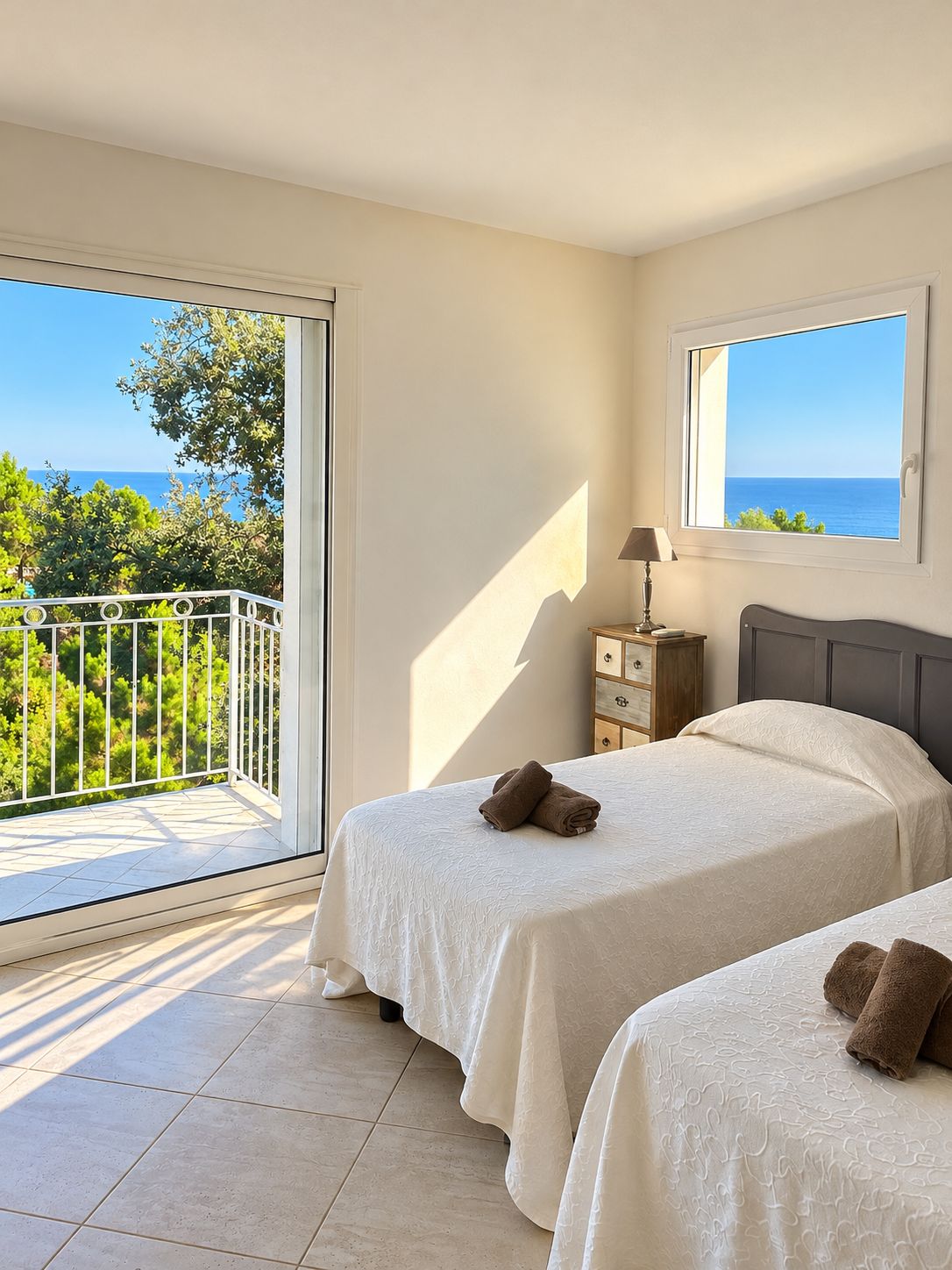 Une chambre avec deux lits, une fenêtre donnant sur la mer et un balcon avec une balustrade.