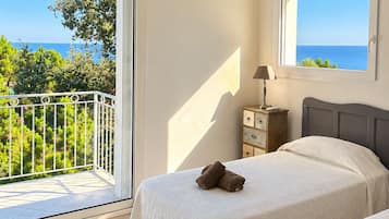 Une chambre avec deux lits, une fenêtre donnant sur la mer et un balcon avec une balustrade.