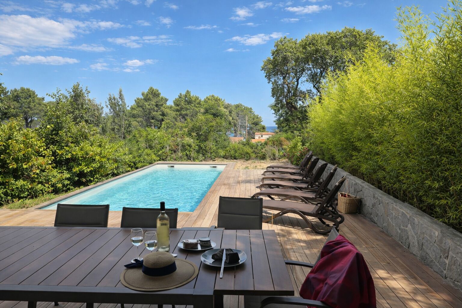 Un área de comedor junto a la piscina con una mesa para dos, una botella de vino y un sombrero.