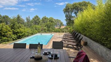 Un área de comedor junto a la piscina con una mesa para dos, una botella de vino y un sombrero.