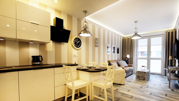 A modern kitchen with white cabinetry, a dining table with chairs, and a living area with a sofa and a coffee table. - Golden Sun Apartments  - Bursztynowe (Kolobrzeg)