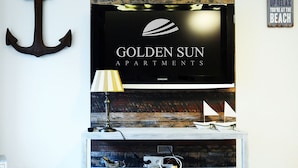 A living room with a television displaying "GOLDEN SUN APARTMENTS" and a decorative anchor on the wall. - Golden Sun Apartments  - Bursztynowe (Kolobrzeg)