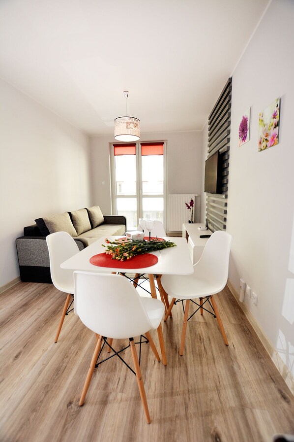 Un coin repas moderne avec une table blanche, quatre chaises blanches et un set de table rouge.