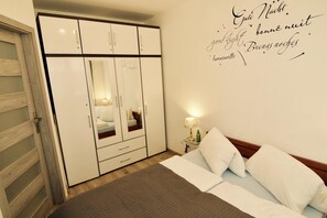 Une chambre à coucher comprenant un lit, une armoire, une table de chevet avec une lampe, et un mur orné d’une inscription décorative.
