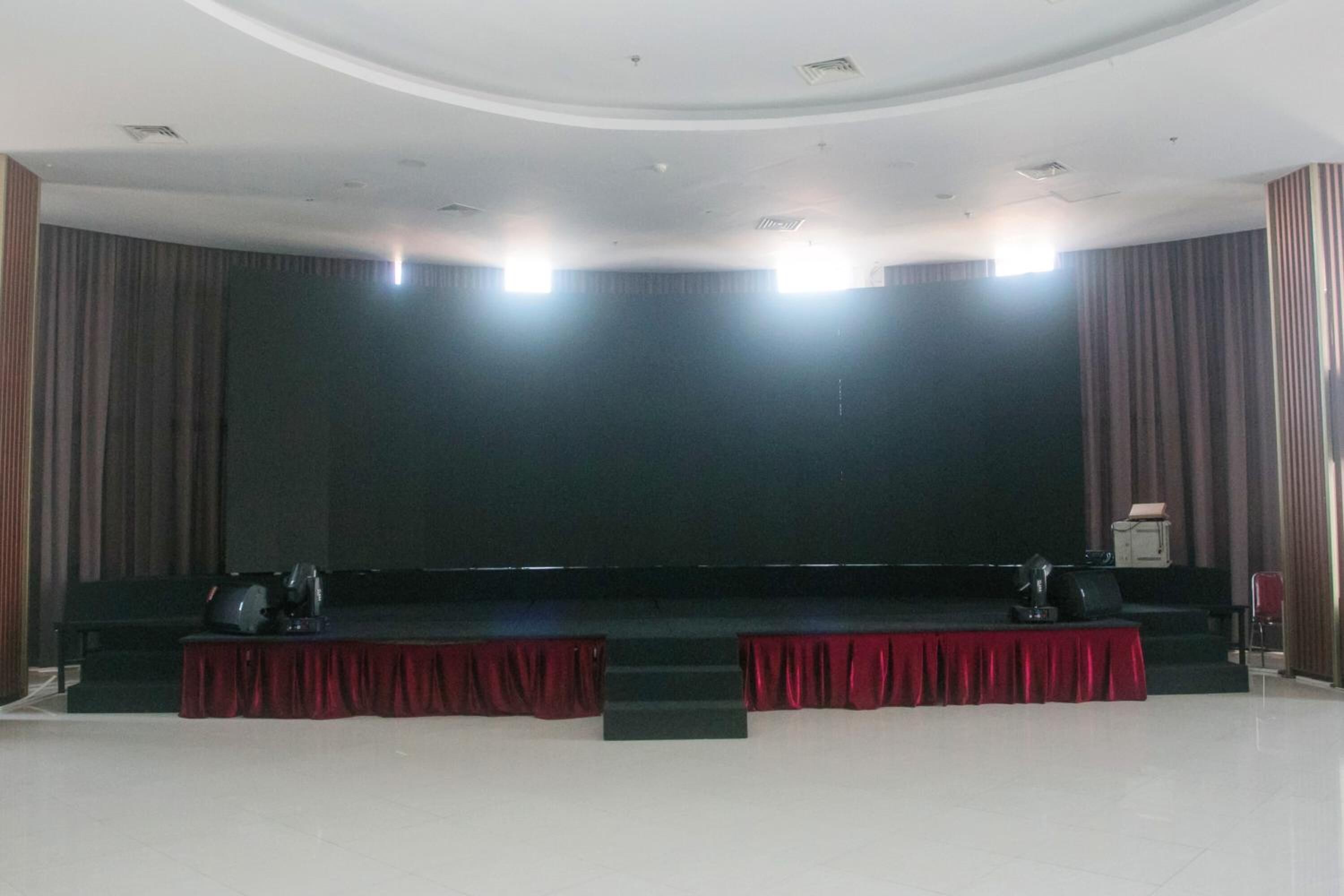 Un auditorio grande y vacío con un escenario, cortinas rojas y un televisor de pantalla plana.