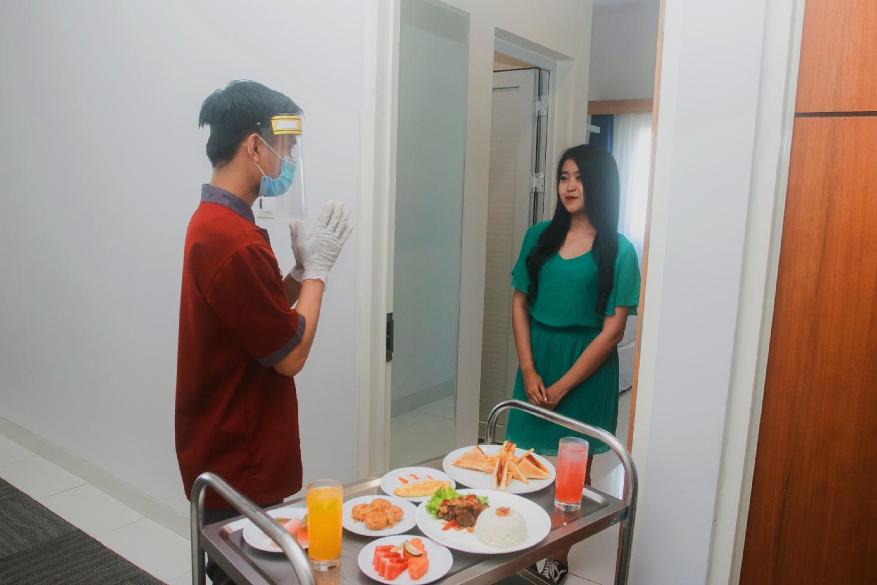 Habitación de hotel con un carrito de comidas que contiene platos de comida, un vaso de jugo de naranja y una bebida rosada.