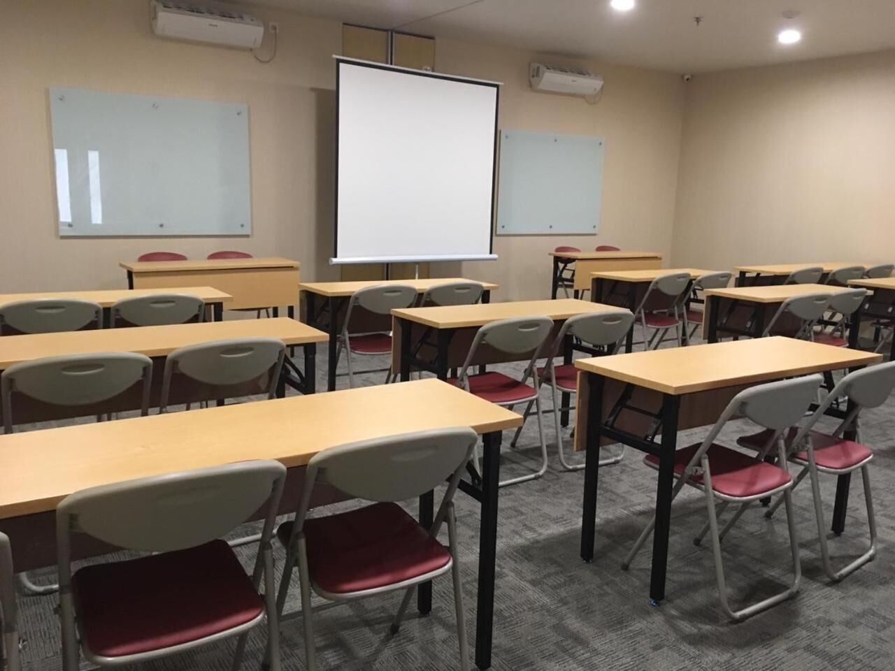 A classroom with rows of desks and chairs, a whiteboard, and a projector screen.