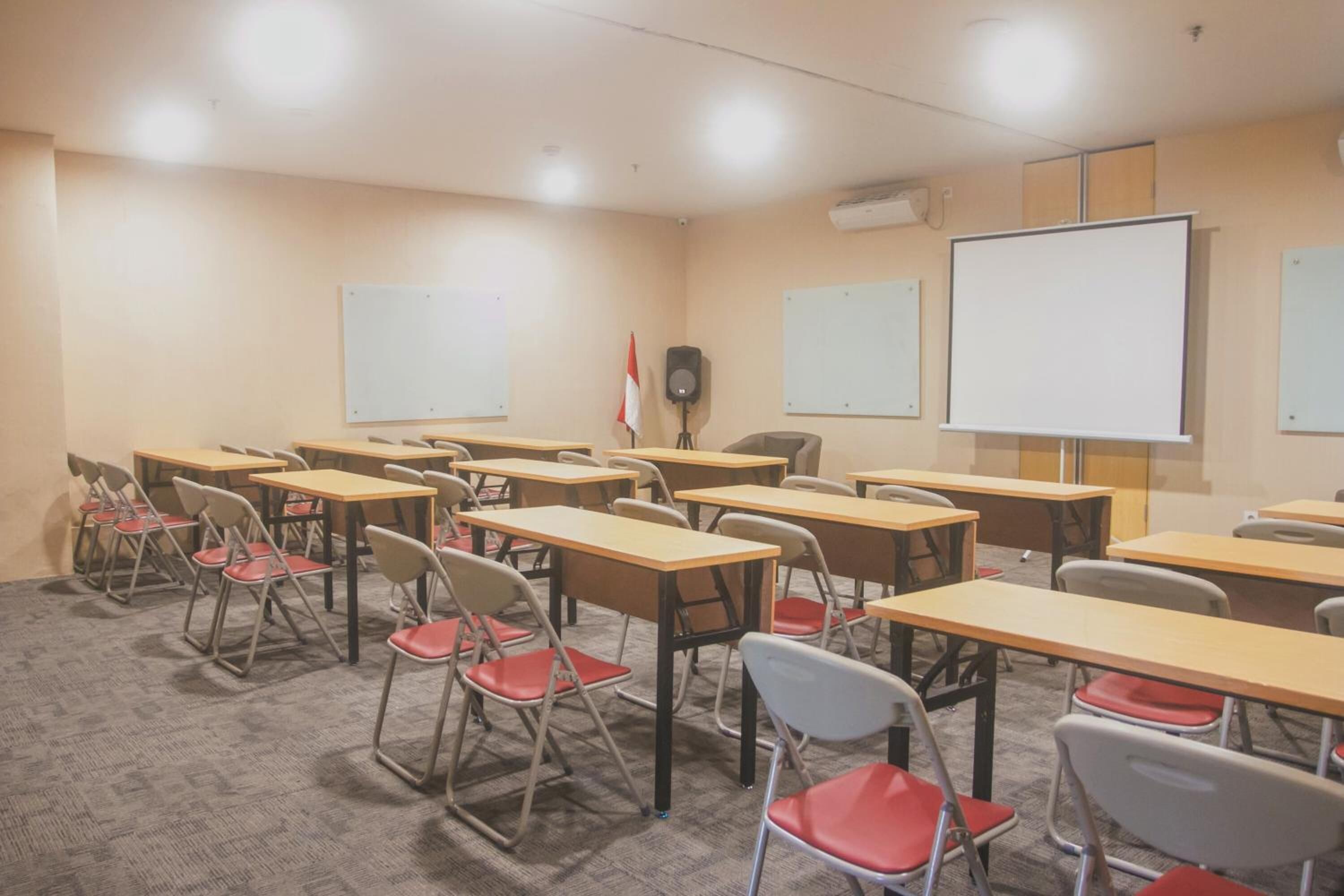 Un aula con escritorios, sillas, pizarras blancas y un altavoz.