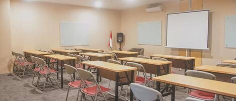 Un aula con escritorios, sillas, pizarras blancas y un altavoz.