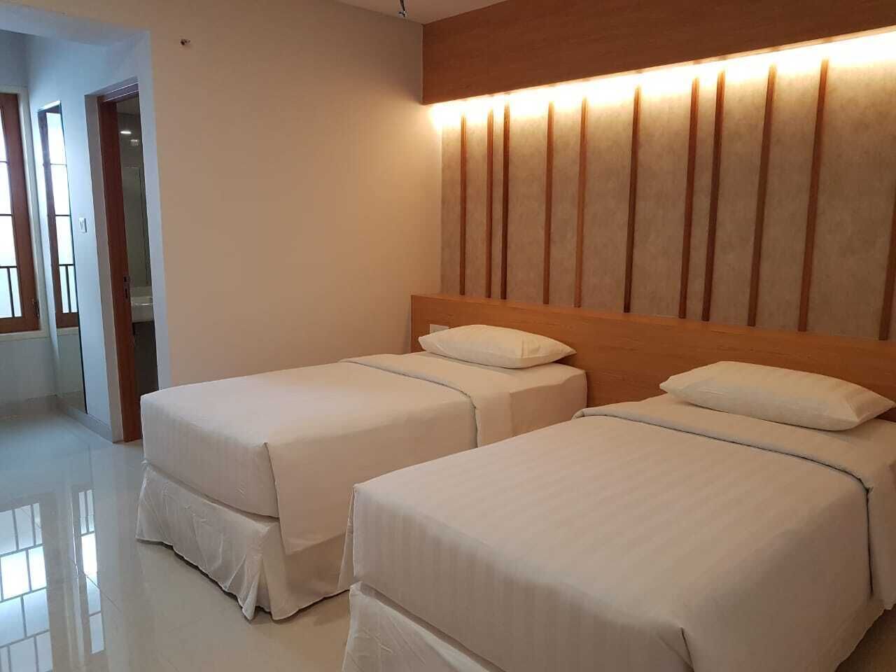 Une chambre d’hôtel avec deux lits, une tête de lit en bois et un panneau mural éclairé.