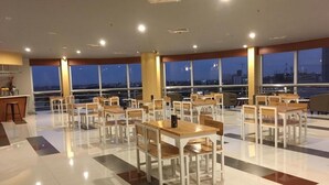 Un vaste espace dédié à la salle à manger, avec de nombreuses tables et chaises, de grandes fenêtres offrant une vue sur la ville, et un aménagement propre et moderne.
