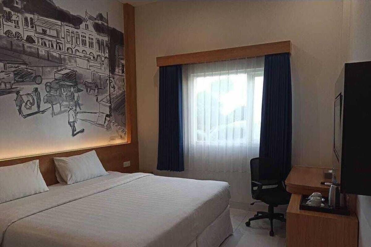 A hotel room with a large bed, a desk with a chair, a flat-screen TV, and a window with curtains.