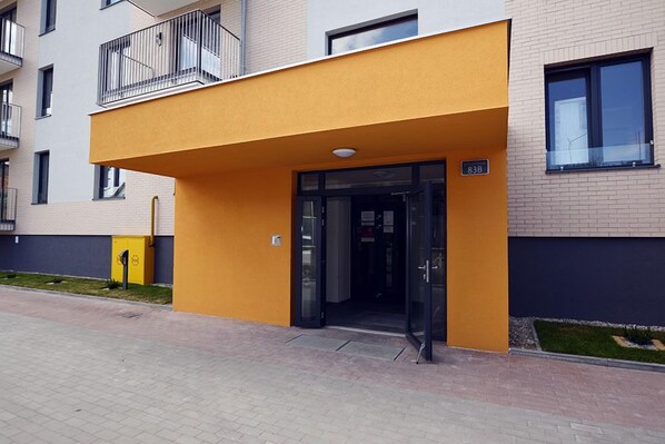 A modern building with a yellow facade, a glass entrance, and a balcony with metal railings.