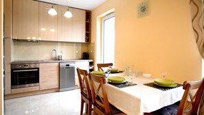 Cozinha moderna com armários de madeira, máquina de lavar louça e forno. Uma mesa de jantar posta com pratos e copos verdes.