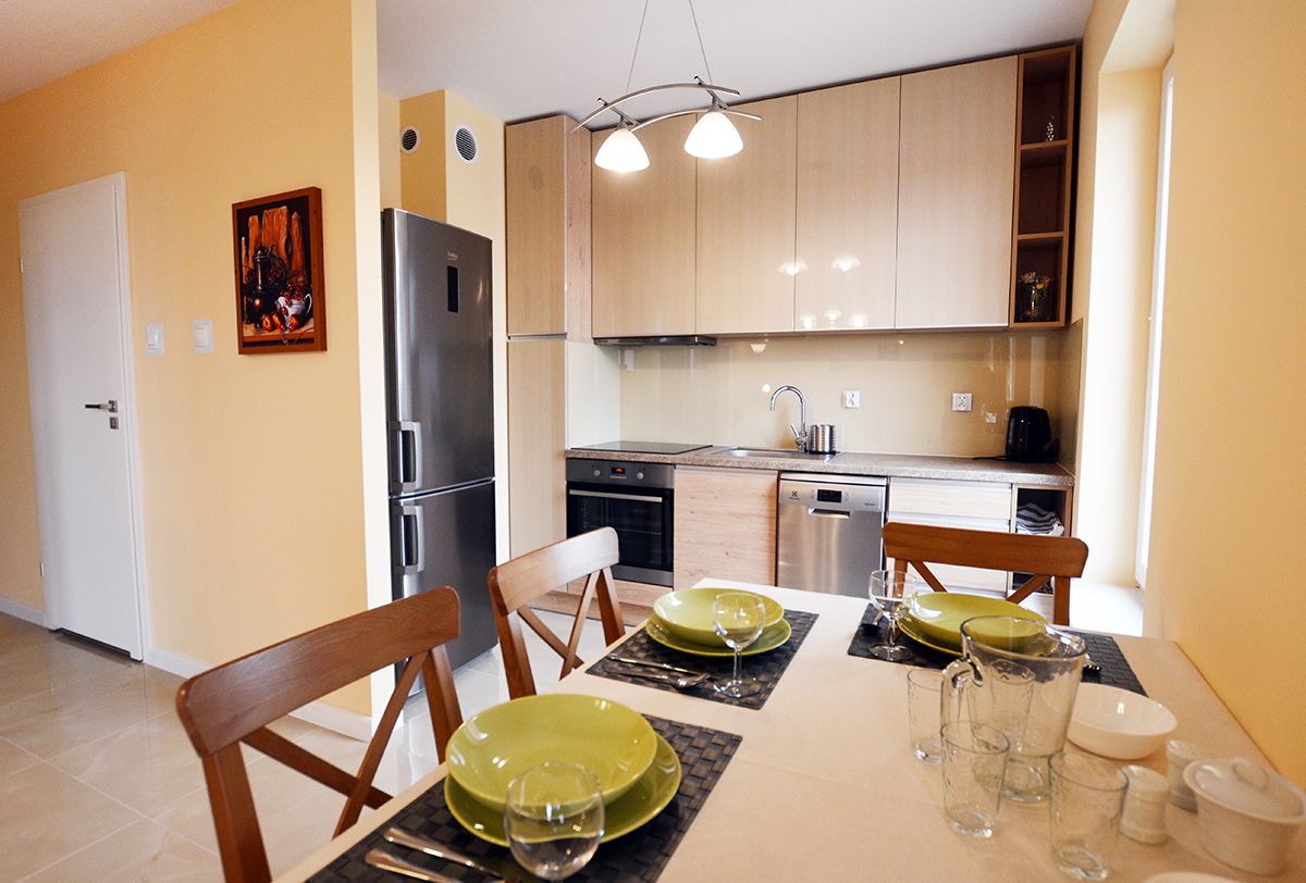 Una cocina moderna con armarios de madera, un refrigerador de acero inoxidable y un comedor con una mesa preparada para cuatro personas.