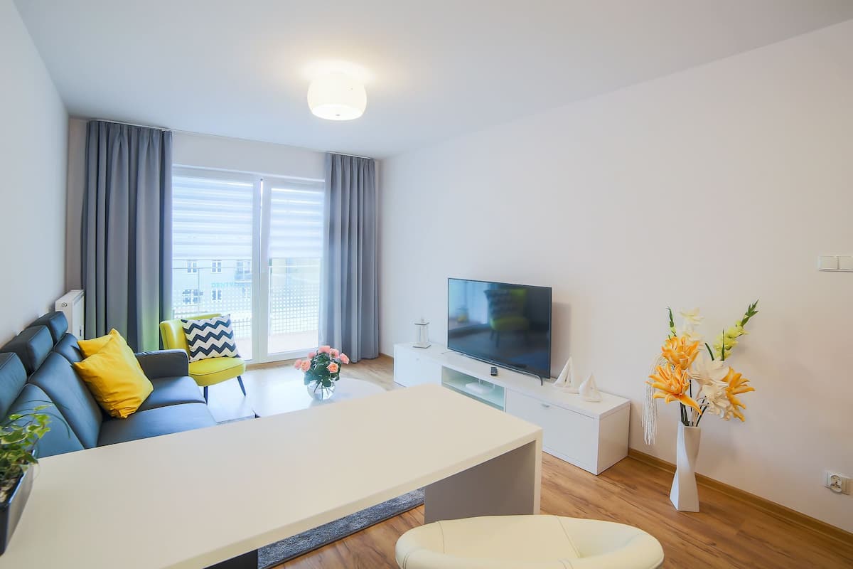 A modern living room with a sofa, a flat-screen TV, a dining table, and a vase of flowers.