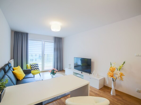 A modern living room with a sofa, a flat-screen TV, a dining table, and a vase of flowers.