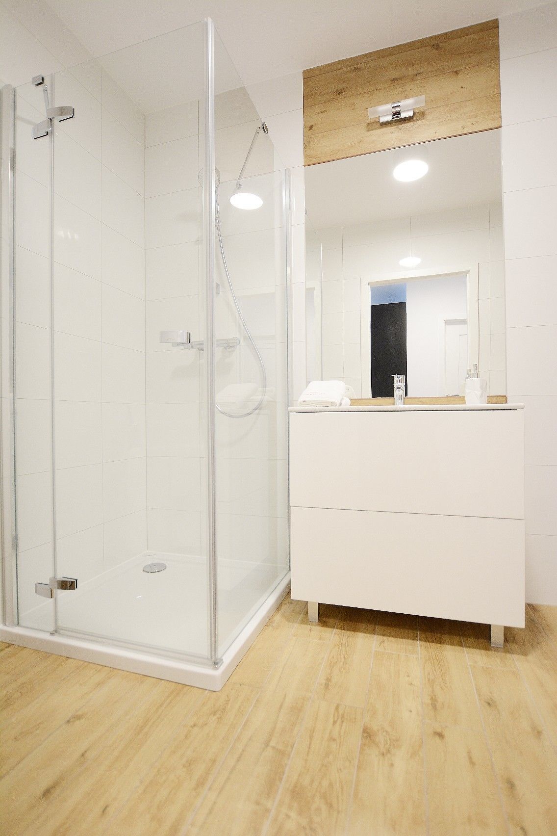 A modern bathroom with a glass-enclosed shower, a white vanity with a mirror, and wooden flooring.