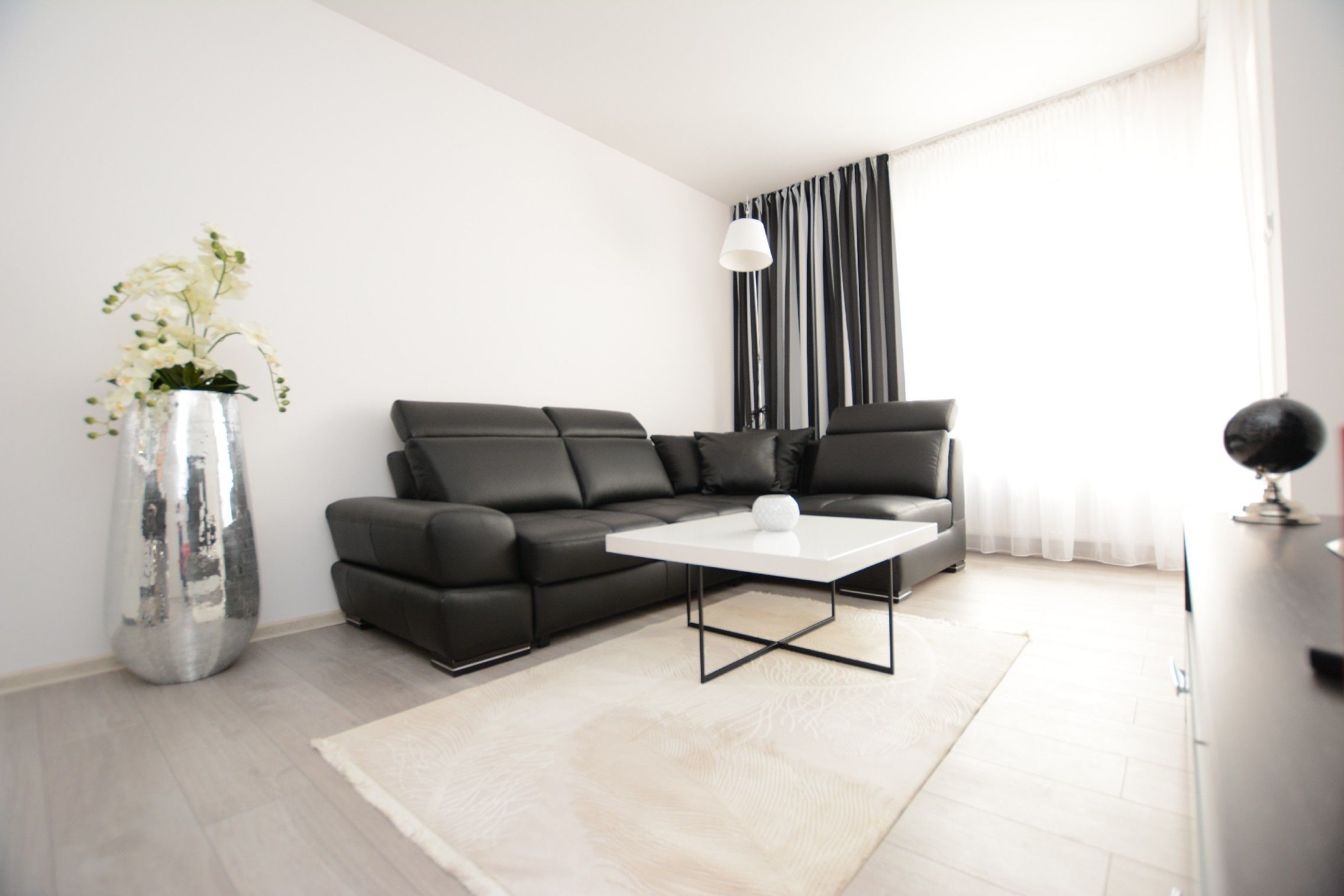 Una sala de estar moderna con un sofá seccional negro, una mesa de centro blanca y un gran ventanal con cortinas blanco y negro.